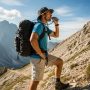 Hiker sipping from hydration tube on mountain trail with tactical backpack.