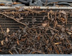 Close-up view of automobile radiator blocked by leaves and road debris causing cooling problems