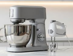 Stand mixer with stainless steel bowl on kitchen counter next to compact hand mixer showing size comparison