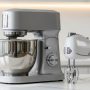 Stand mixer with stainless steel bowl on kitchen counter next to compact hand mixer showing size comparison