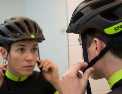 Person adjusting bike helmet side straps to form a V shape under the ears while looking in a mirror