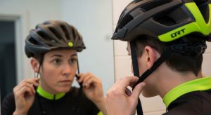 Person adjusting bike helmet side straps to form a V shape under the ears while looking in a mirror