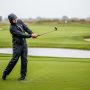 Golfer wearing rain pants swinging on a wet golf course