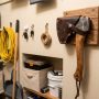 A compact hatchet with a leather sheath mounted on a wooden wall rack inside a small apartment utility closet