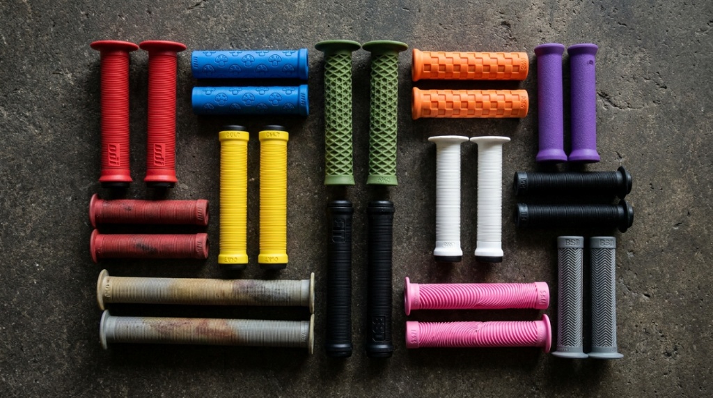 Assortment of colorful flanged and flangeless BMX grips displayed on concrete.