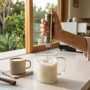 Person using an electric milk frother to foam milk in a kitchen.