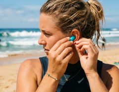 on beach inserting reusable waterproof ear plugs before heading into the ocean.