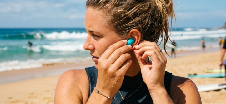 on beach inserting reusable waterproof ear plugs before heading into the ocean.