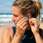 on beach inserting reusable waterproof ear plugs before heading into the ocean.