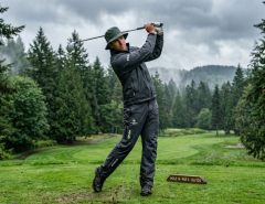 Golfer wearing a waterproof rain jacket swinging on an overcast course.