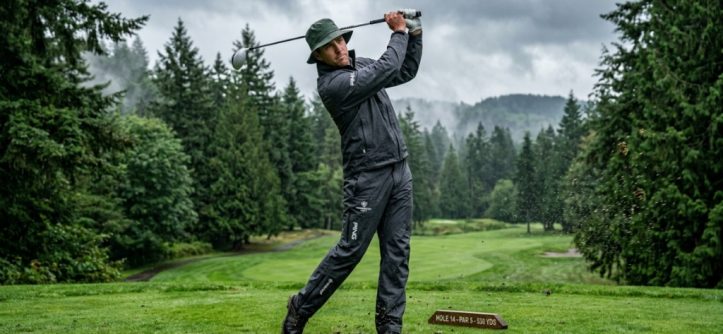 Golfer wearing a waterproof rain jacket swinging on an overcast course.