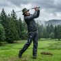 Golfer wearing a waterproof rain jacket swinging on an overcast course.