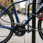 Cyclist securing a bicycle with a heavy-duty U-lock to a metal rack outdoors.