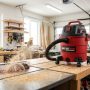 Red shop vacuum cleaning sawdust off a messy workshop floor.